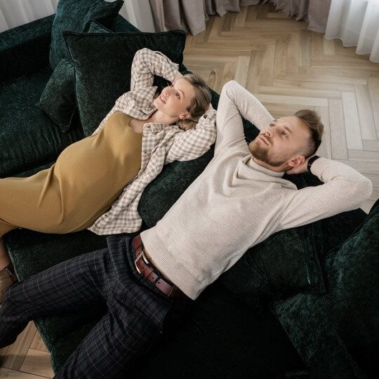 A pregnant couple laid back on a dark green sofa.
