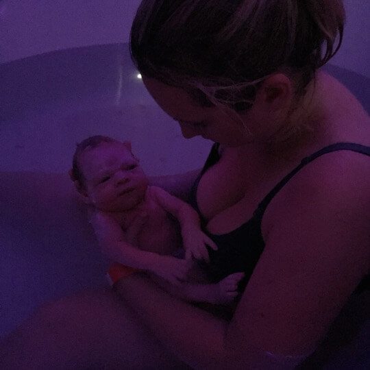 A dark photo of a woman holding a baby in the water having just given birth.
